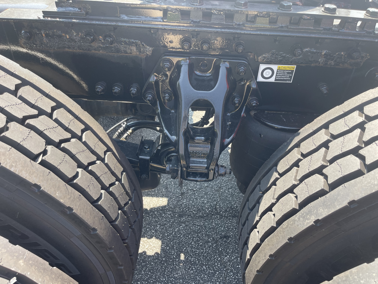 Kenworth T680 chassis area showing rear suspension/axle hanger and dual rear tires with mid-frame coupling and warning sticker visible.