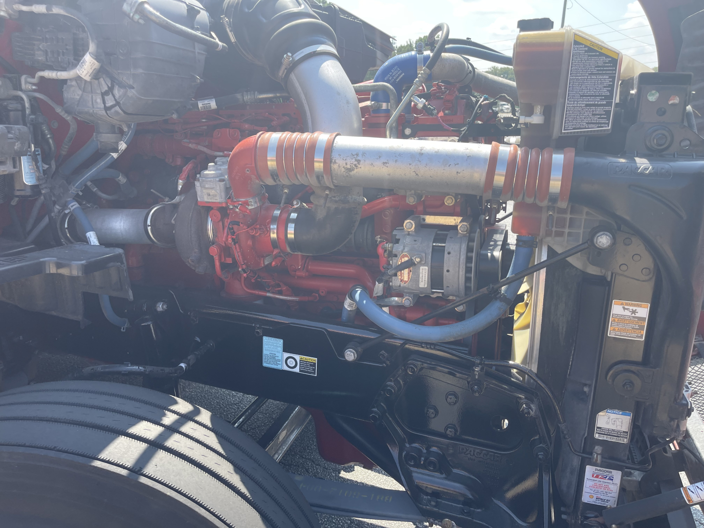 Kenworth engine bay showing diesel engine with red components, hoses, and blue wiring harness.