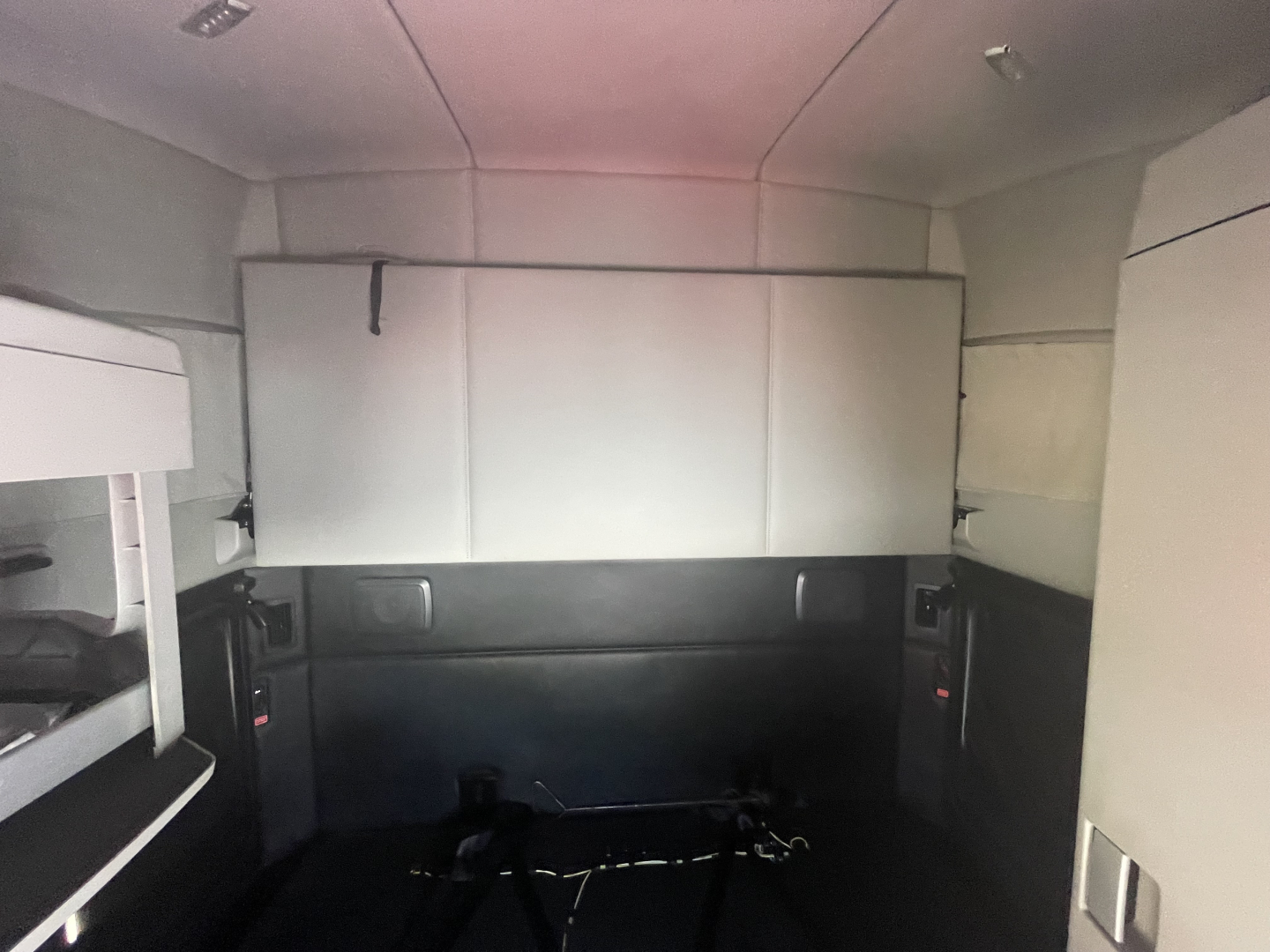 Kenworth T680 sleeper cab interior cargo area with ceiling panels and side storage, rear view showing empty floor space.