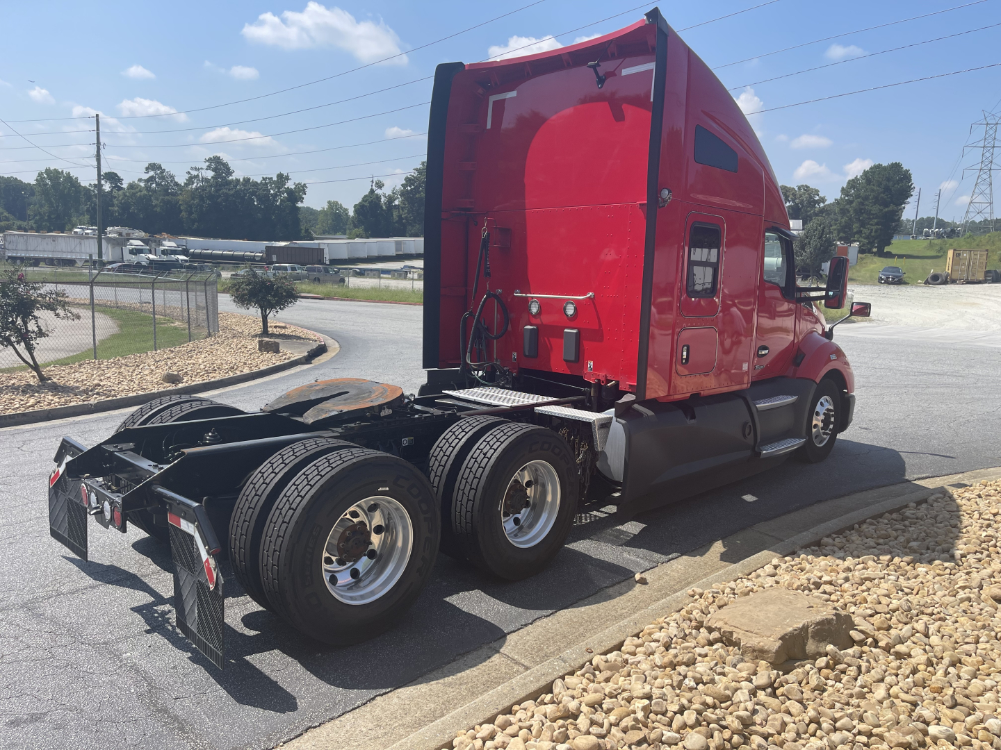 Truck rear view showing red Kenworth T680 sleeper cab with dual rear axles and fifth-wheel, black fenders, and round fuel tanks.