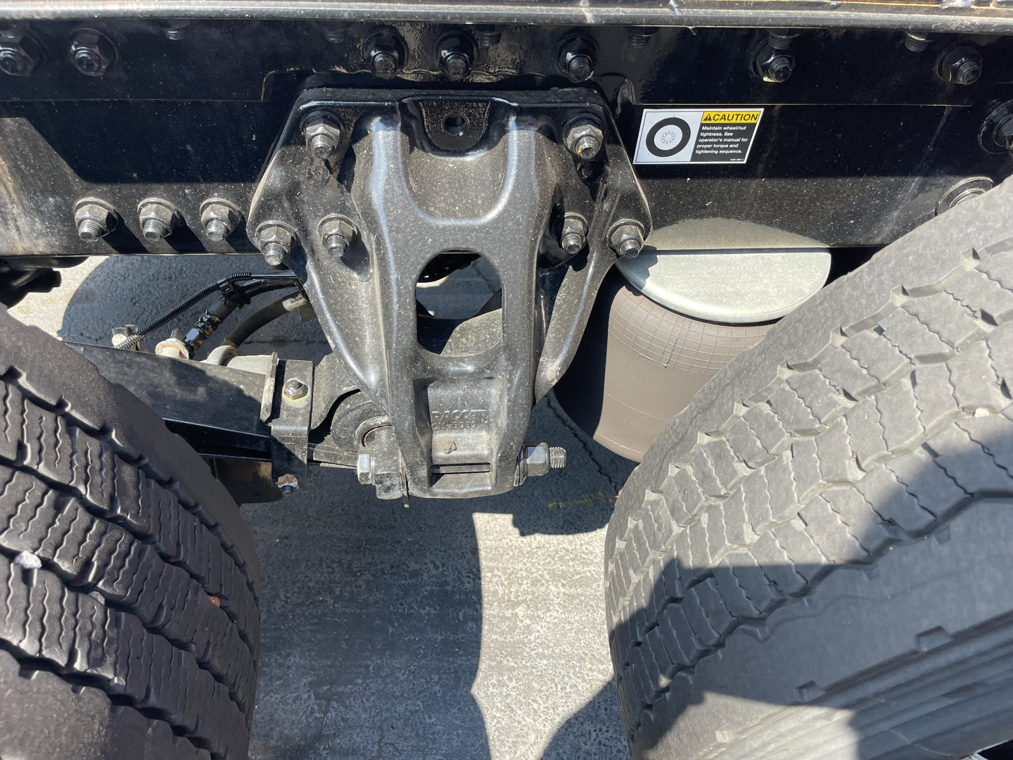 Kenworth T680 truck undercarriage showing drivetrain hanger and dual rear axles with leaf springs and tires visible.