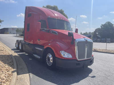 Red 2022 Kenworth T680 semi-truck in a parking lot shows cab and sleeper, with chrome grille and side mirrors; no visible text on the truck.