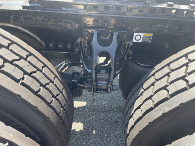 Kenworth T680 chassis area showing rear suspension/axle hanger and dual rear tires with mid-frame coupling and warning sticker visible.