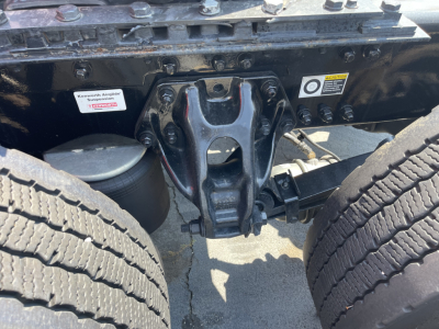 Kenworth T680 chassis center showing fifth wheel and suspension components with dual rear tires and warning labels visible.