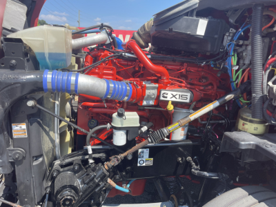 Kenworth T680 engine bay showing CE15 engine with red intake manifold, blue silicone turbo boot, fuel filters, hoses, and wiring harnesses.
