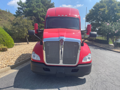 Kenworth T680 front view showing large chrome grille, red cab, black bumper, and side mirrors.