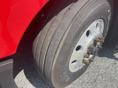 Front dual rear wheel assembly of a red Kenworth T680 truck showing tire sidewalls and wheel with lug nuts in view.