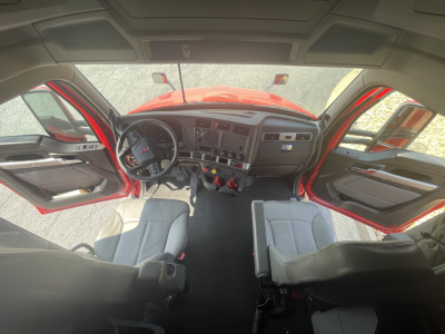 Kennworth T680 cockpit view with open doors showing driver and passenger seats, dashboard with controls, steering wheel, center console, and windshield.