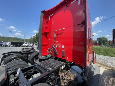 Kenworth T680 cab with bright red sleeper area, rear view showing chassis and fifth wheel, side mirror in view.