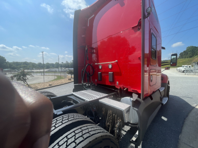 Kenworth T680 truck cab rear-side view showing red sleeper cab, fuel steps, rear wheels, and chassis with visible metal platforms.
