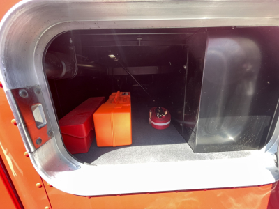 Trunk/storage area of a 2022 Kenworth T680 with two battery boxes and a red circular device visible.