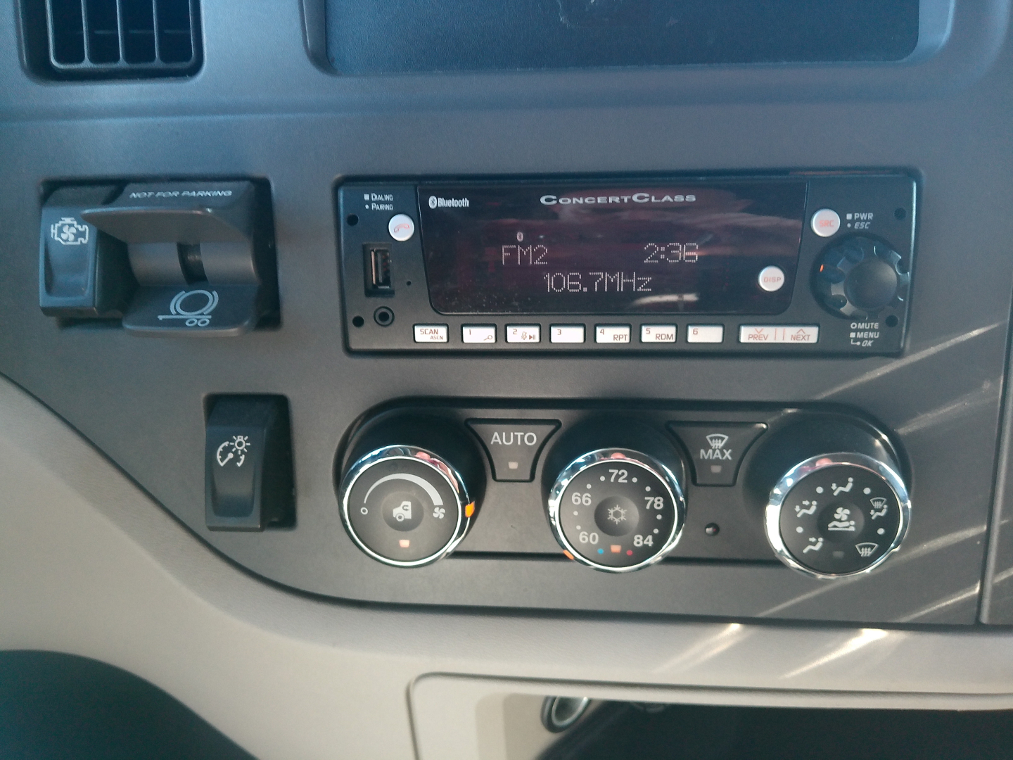 Truck dashboard showing Conrad Class radio FM2 106.7MHz, climate control dials, switch panel, and a dash badge area. Visible text includes 'ConectClass' on the radio, 'FM2 106.7MHz', 'AUTO', and various climate control numbers.
