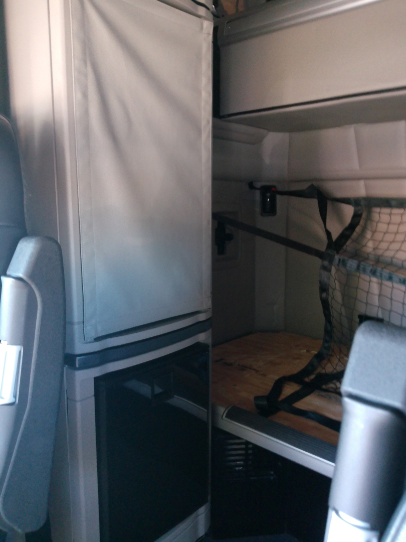 Truck interior cab area of a 2023 Peterbilt 579 showing a bunk area and storage cabinet with a netted side pocket.