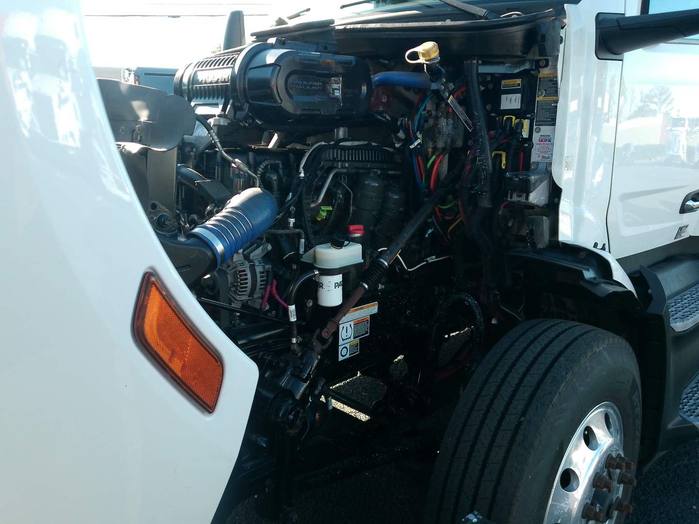 Peterbilt 579 engine bay view with exposed components, hoses, wiring and air intake; front wheel and fender visible.