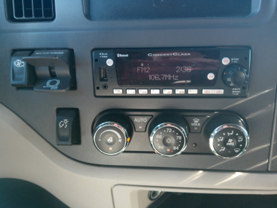 Truck dashboard showing Conrad Class radio FM2 106.7MHz, climate control dials, switch panel, and a dash badge area. Visible text includes 'ConectClass' on the radio, 'FM2 106.7MHz', 'AUTO', and various climate control numbers.