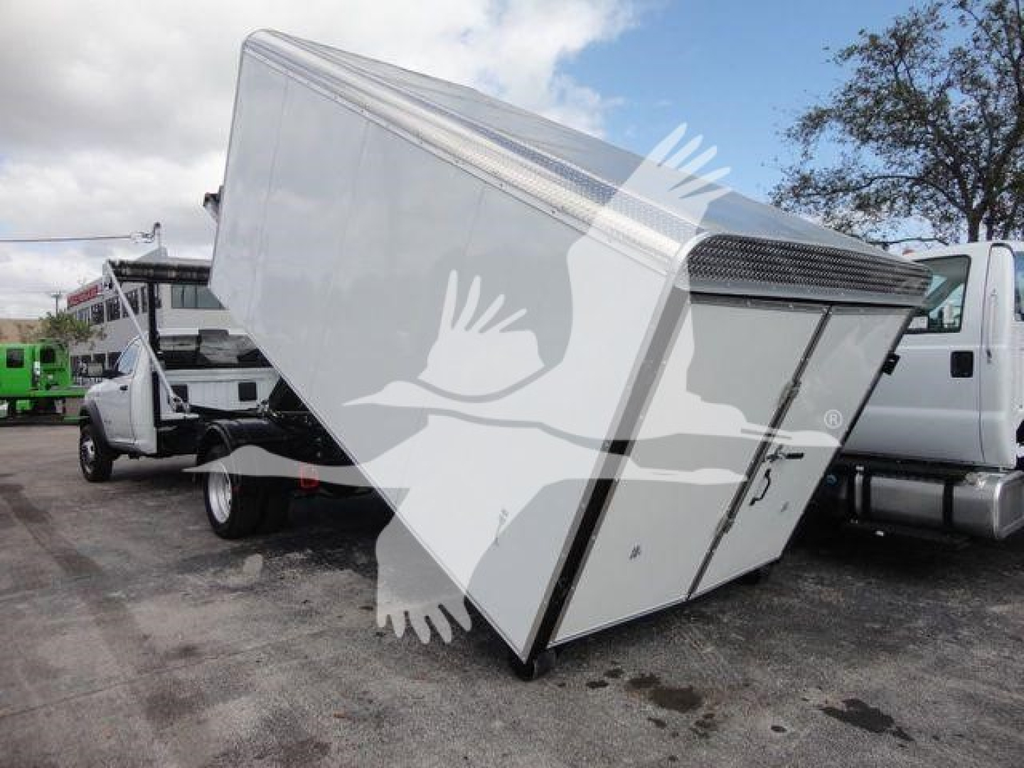 Truck with a tipped white roll-off container on a Ram 5500 chassis, showing a tilted cargo box and adjacent trucks.