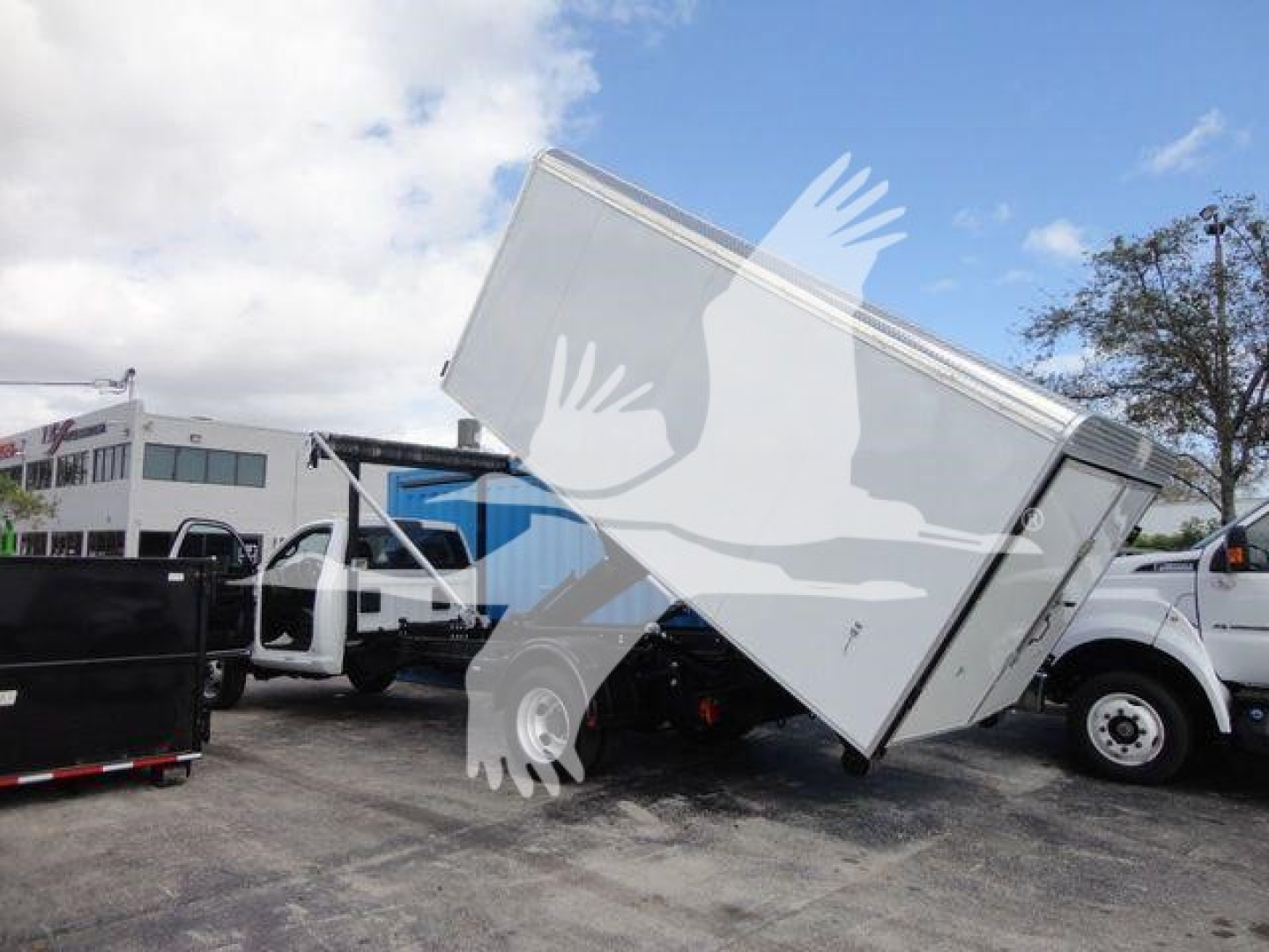 Ram 5500 HD roll-off truck with various equipment in a dealership yard, side view showing off-cab and container body tilted.