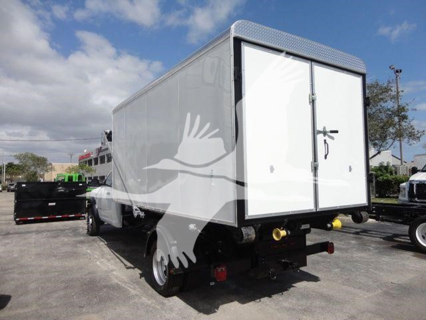 Ram 5500 HD roll-off truck with a white box, rear doors visible, two yellow hitch pins, and a spare wheel beneath. No visible branding text legible on the image itself.