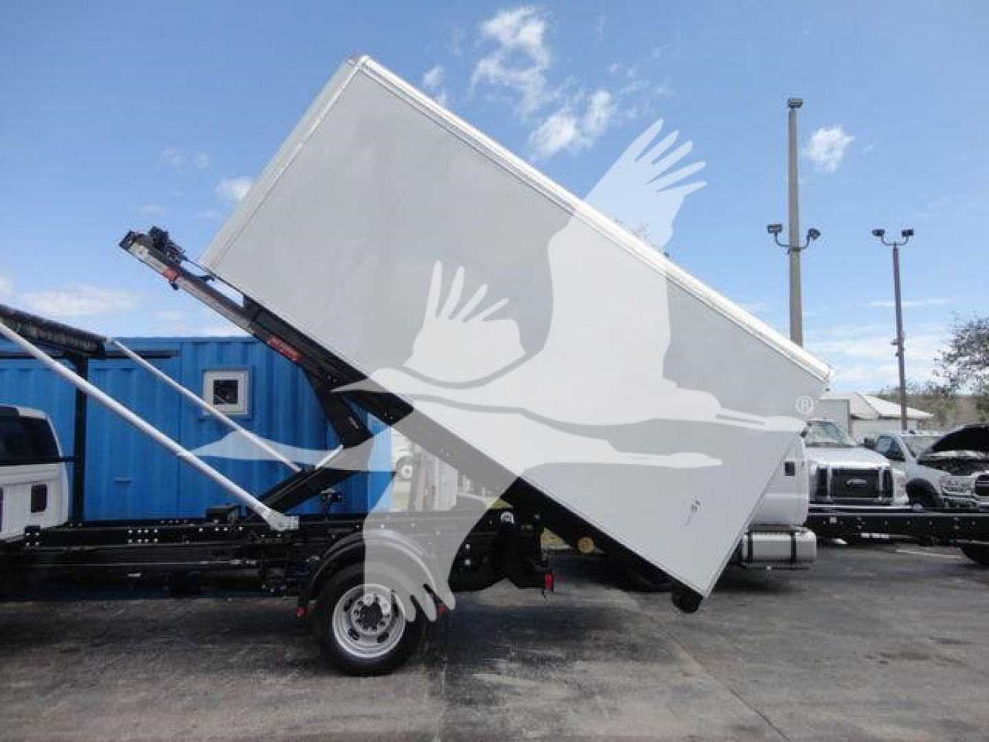 Ram 5500 HD roll-off truck bed tilted on a trailer with hydraulic lift and white cargo container.