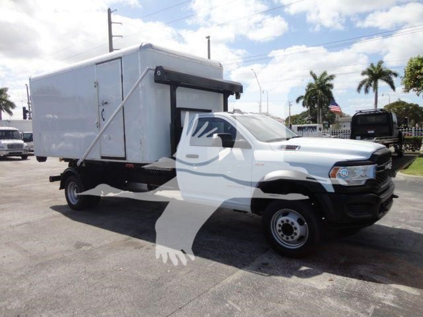 Ram 5500 HD roll-off truck showing a white cab and a large white utility box mounted on the chassis.