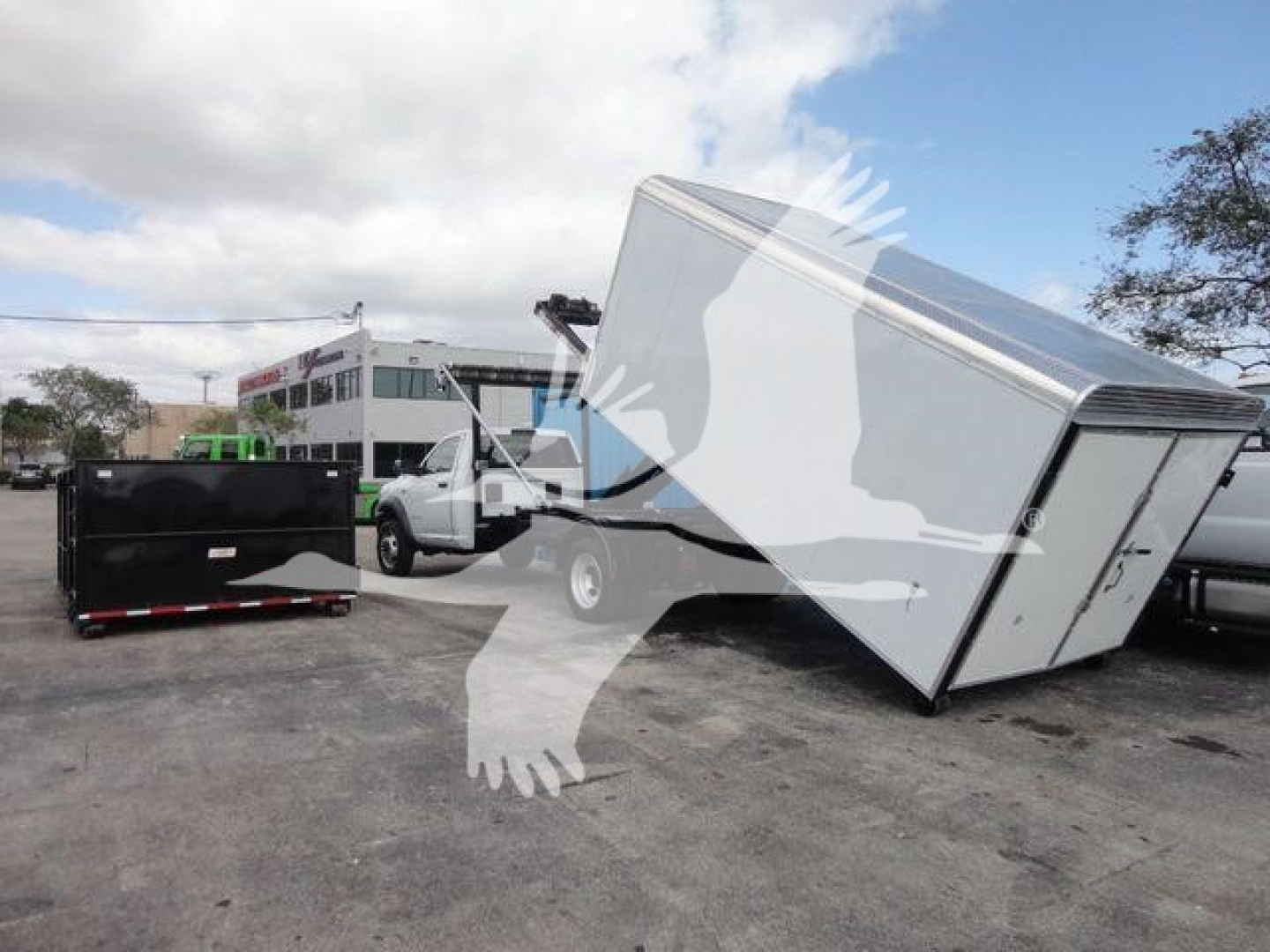 Ram 5500 HD rolloff truck with a tilted metal box and nearby equipment in lot; no legible model-year text visible on the image.