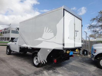 Ram 5500 HD roll-off truck with a large rectangular cargo box on the back. The box has a side door and a rear hatch; the truck is white with black chassis and dual rear wheels.