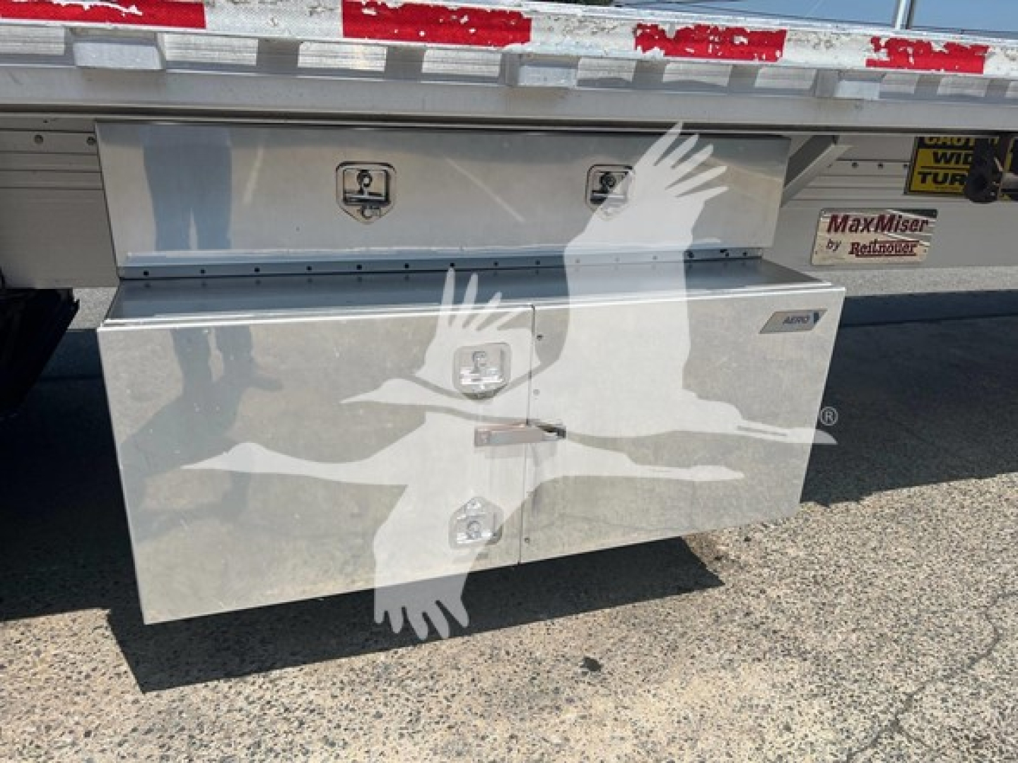Flatbed trailer rear toolbox on a 2015 Reitnouer Maxmiser, aluminum toolbox with multiple latches and a clip, mounted under the trailer deck.