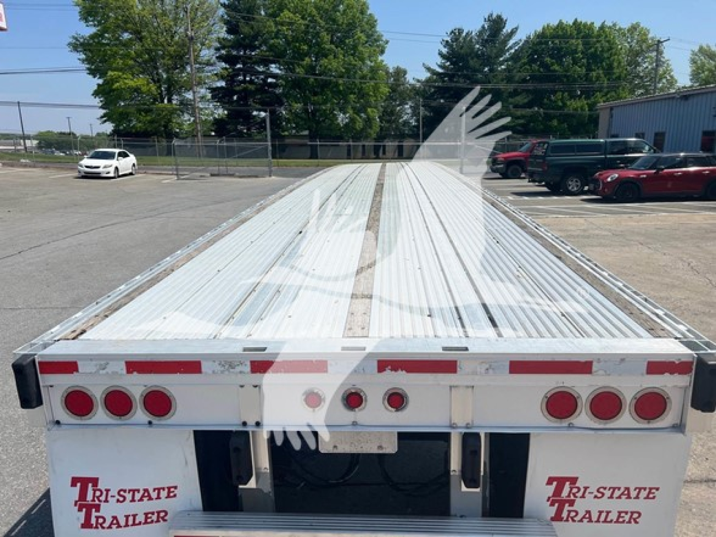 Flatbed trailer showing long white corrugated deck with rear lights and bumper; Tri-State Trailer logo on back. 2015 Reitnouer Maxmiser trailer.