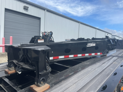Trailer chassis showing Load King logo, heavy steel frame, near-black paint, side marker reflectors, and landing gear in a parking lot.