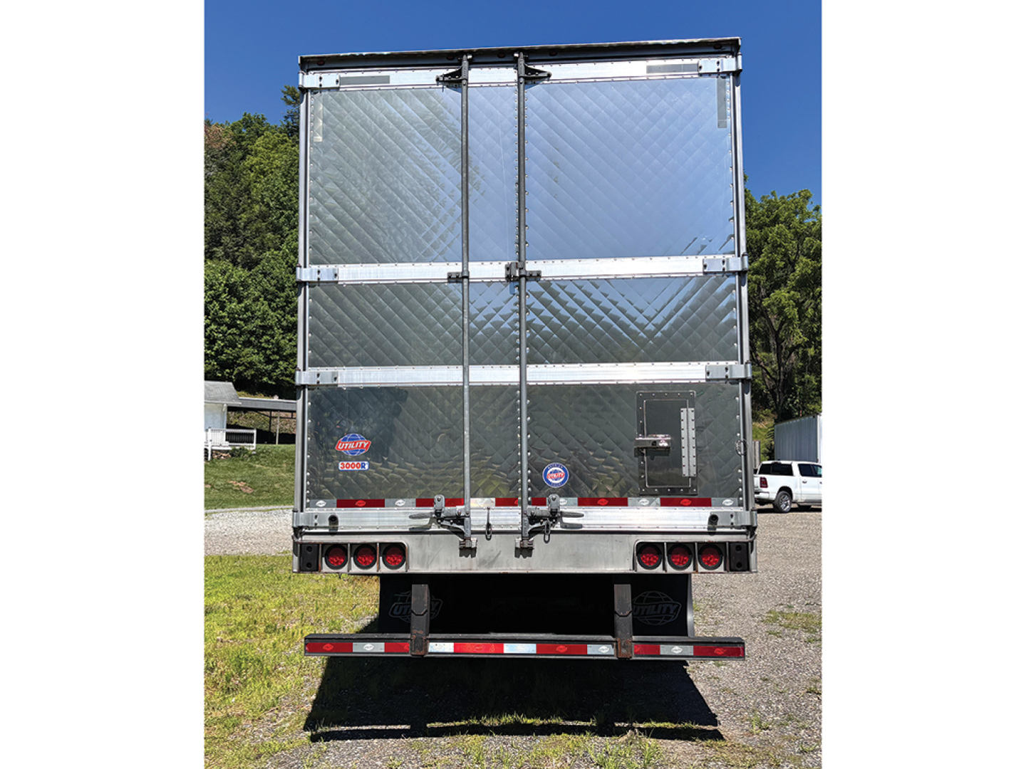 Rear view of a 2024 Utility 3000R trailer with diamond plate aluminum panels, dual rear doors, and reflective bumper; standard reefer trailer features visible branding decals and taillights.