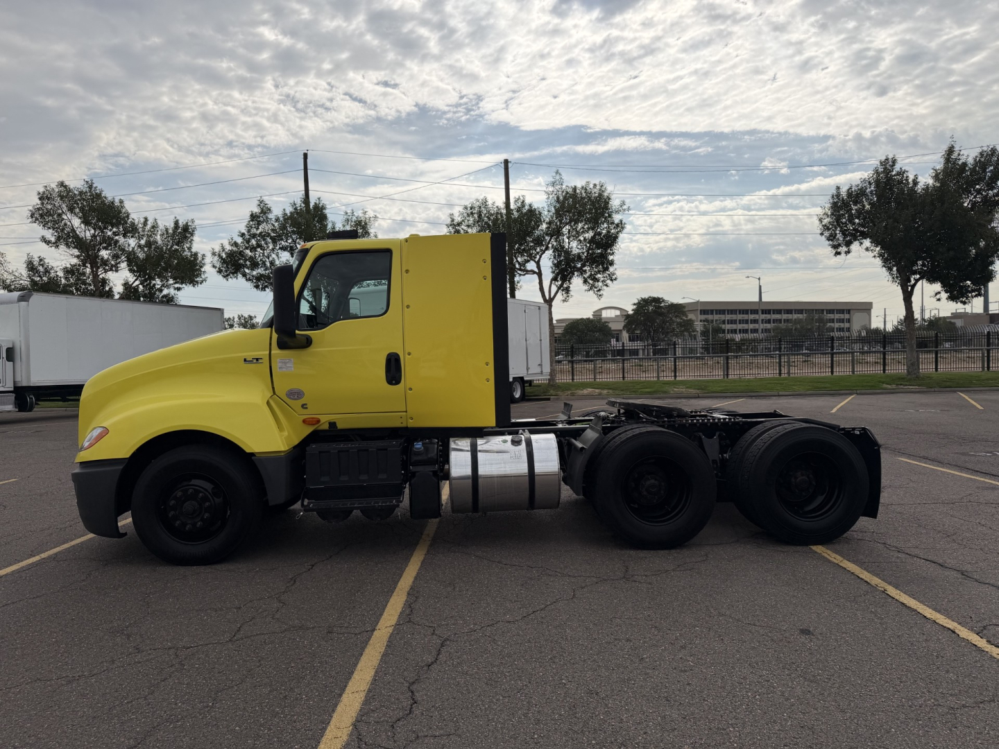 Truck side view showing bright yellow cab and black chassis of a conventional daycab semi-truck.