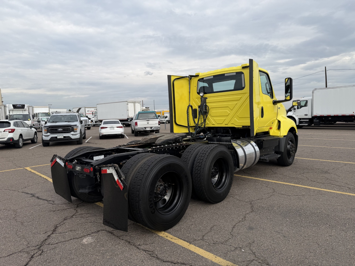 Yellow 2023 International LT625 daycab tractor rear and cab side with chassis and dual rear axles, fuel tank, black mudflaps, and parking lot.