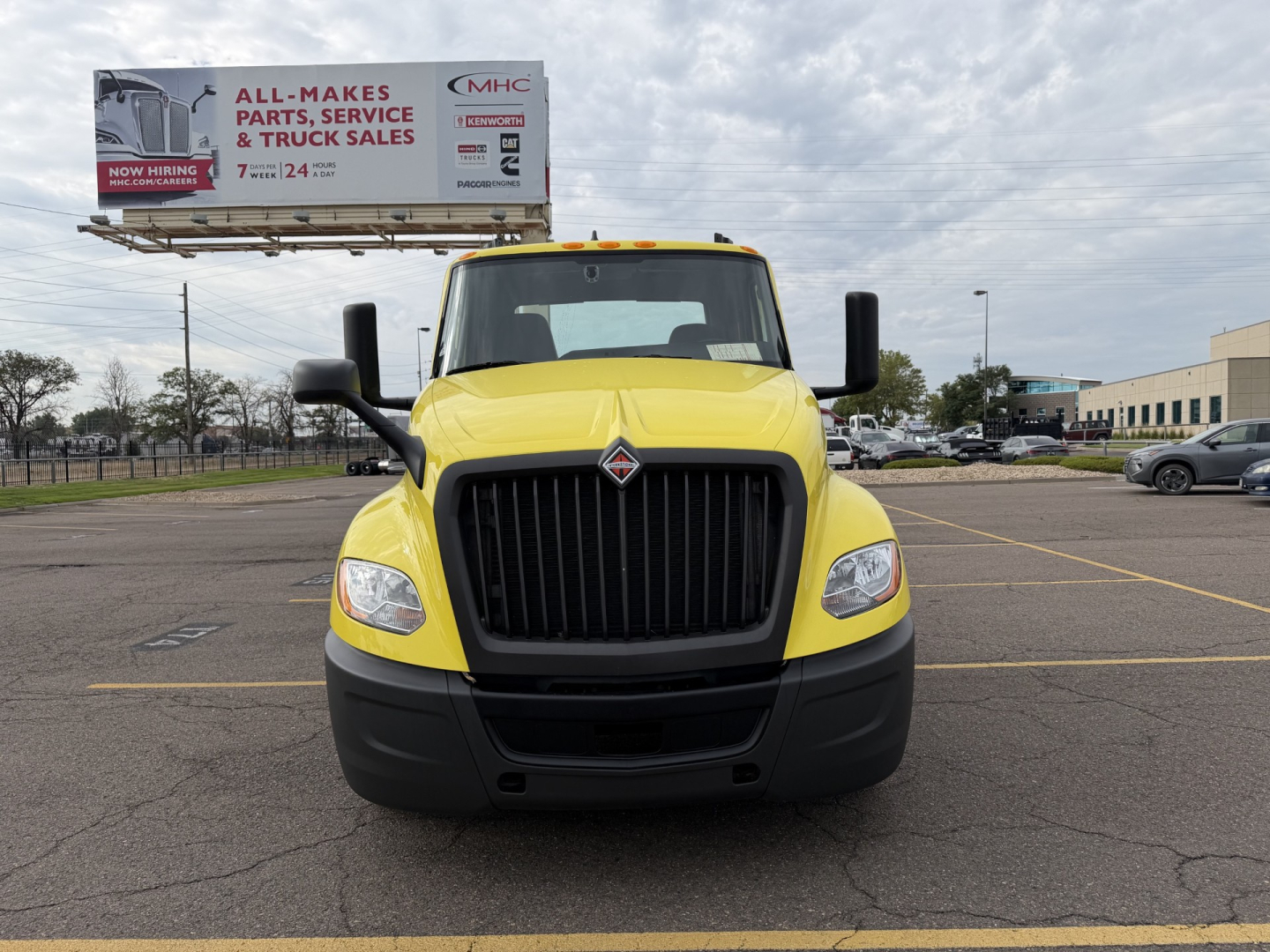 Truck front view of a yellow 2023 International LT625 with black grille and bumper, in a parking lot.