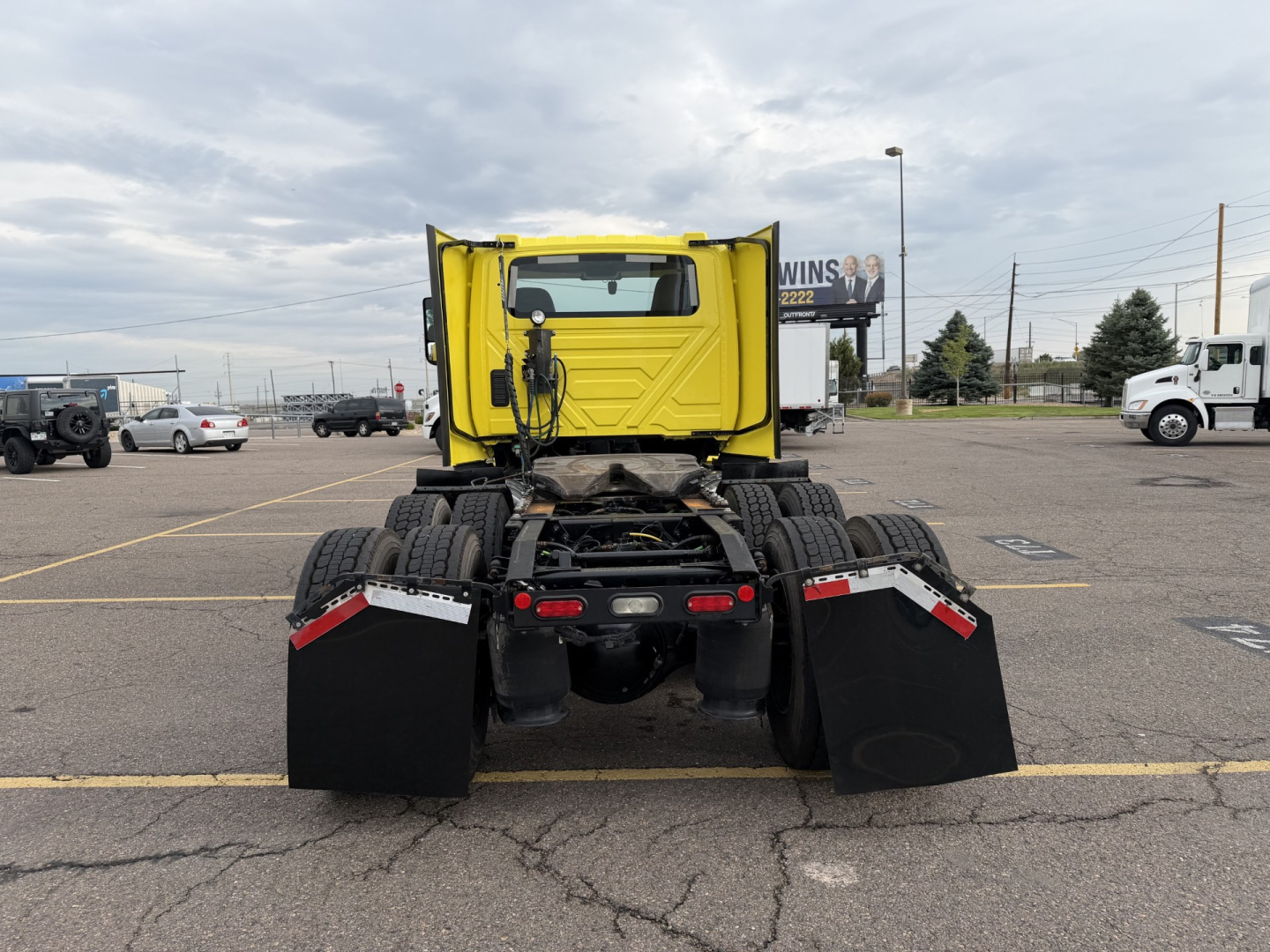 Rear view of a yellow International LT625 daycab truck in a parking lot with mud flaps and dual rear axles.