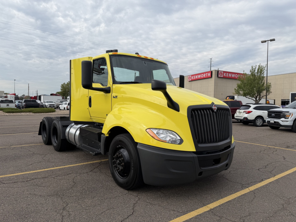 Yellow 2023 International LT625 daycab truck in a parking lot, front-right view showing large black grille, dual rear axles, and black bumper.