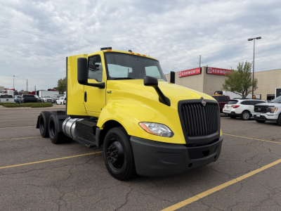 Yellow 2023 International LT625 daycab truck in a parking lot, front-right view showing large black grille, dual rear axles, and black bumper.