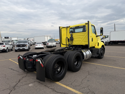 Yellow 2023 International LT625 daycab tractor rear and cab side with chassis and dual rear axles, fuel tank, black mudflaps, and parking lot.