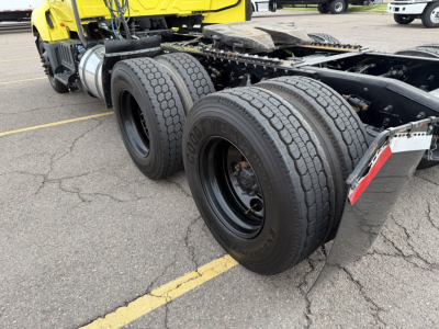 Truck chassis and dual rear wheels of a 2023 International LT625 conventional daycab showing dual 22.5 inch tires, black rims, and yellow cab in background.