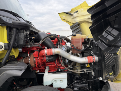 Engine bay of a 2023 International LT625 daycab showing red engine, intercooler piping, coolant reservoir, and yellow cab hood in view