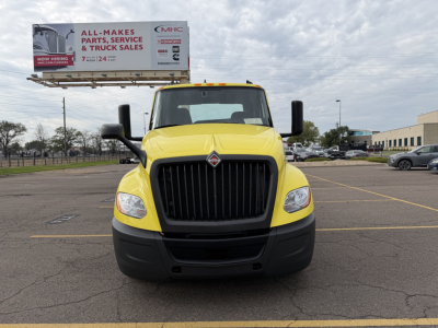 Truck front view of a yellow 2023 International LT625 with black grille and bumper, in a parking lot.