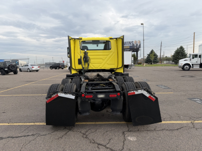 Rear view of a yellow International LT625 daycab truck in a parking lot with mud flaps and dual rear axles.