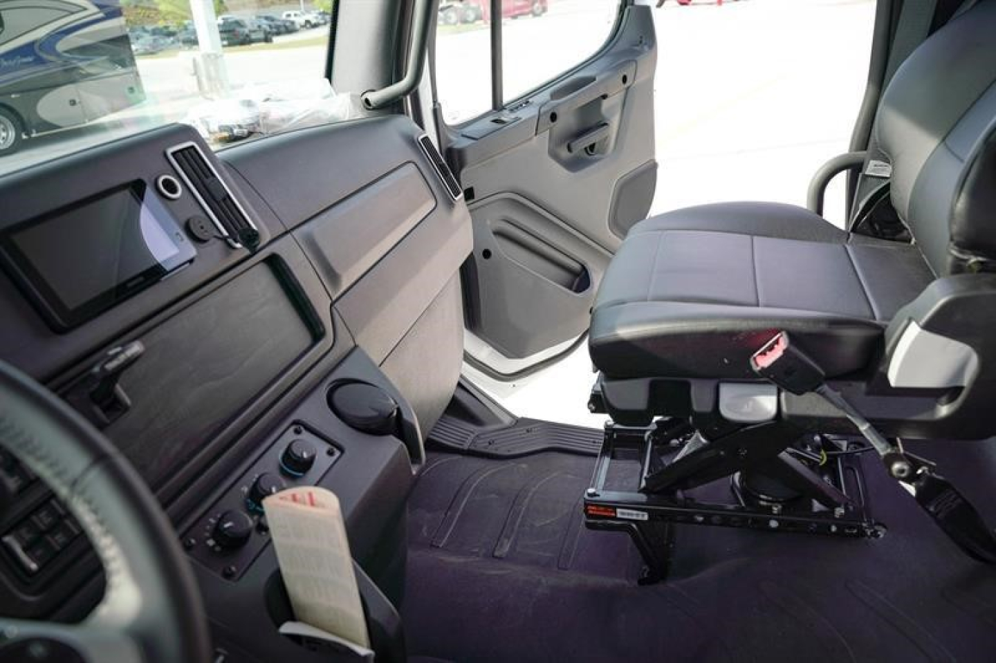 Truck cabin interior showing driver's seat and open passenger door area; instrument panel, controls, and floor mats visible.