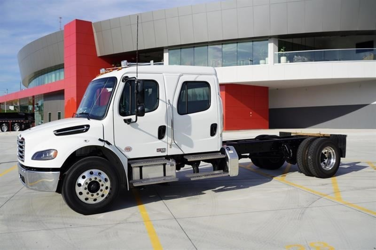 Truck cab and chassis showing Freightliner M2 106 Plus with white dual cab and chassis frame in a dealership lot.
