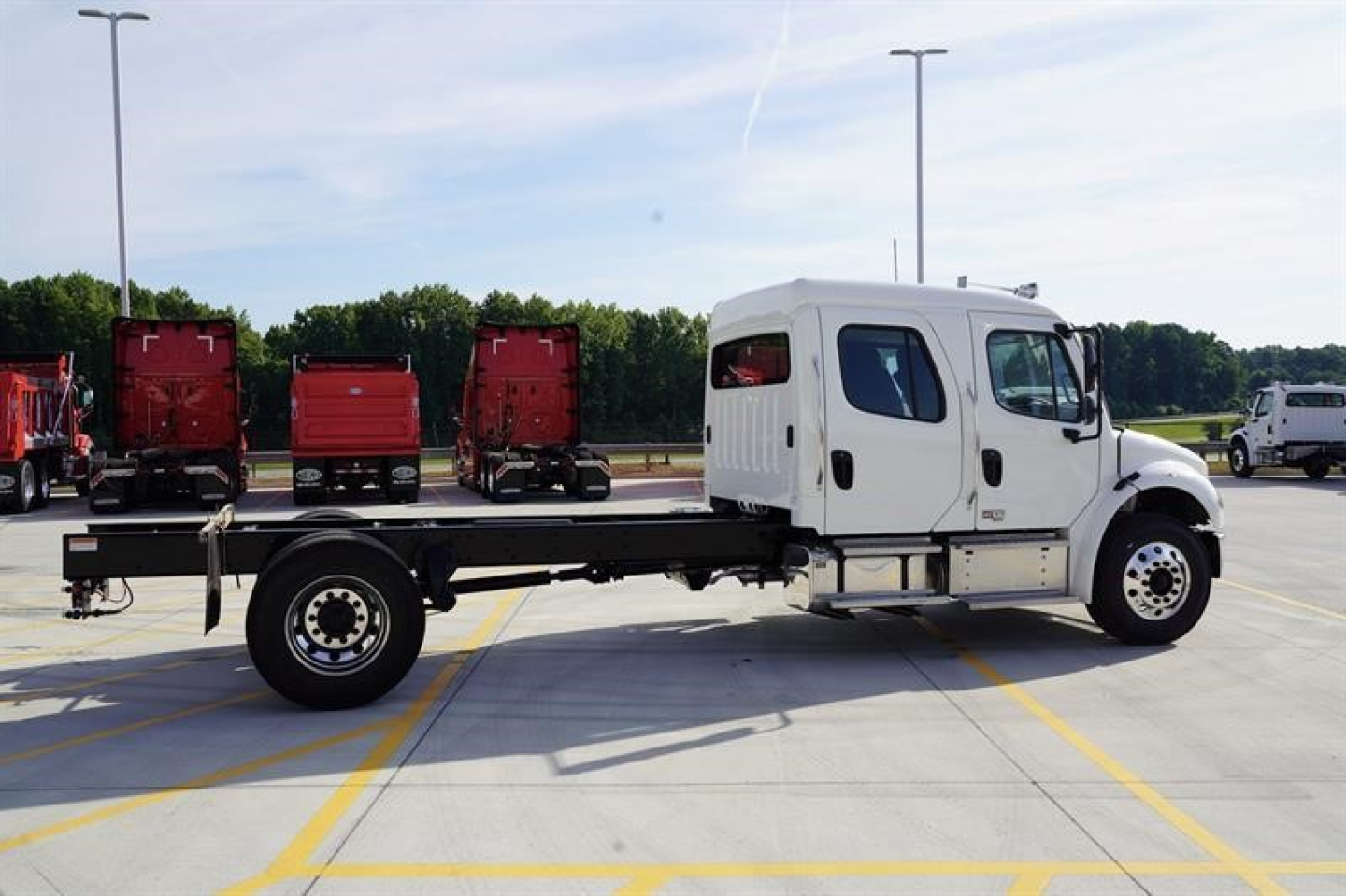 Freightliner M2 106 Plus cab and chassis in parking lot, side view, white cab with flatbed chassis and black frame