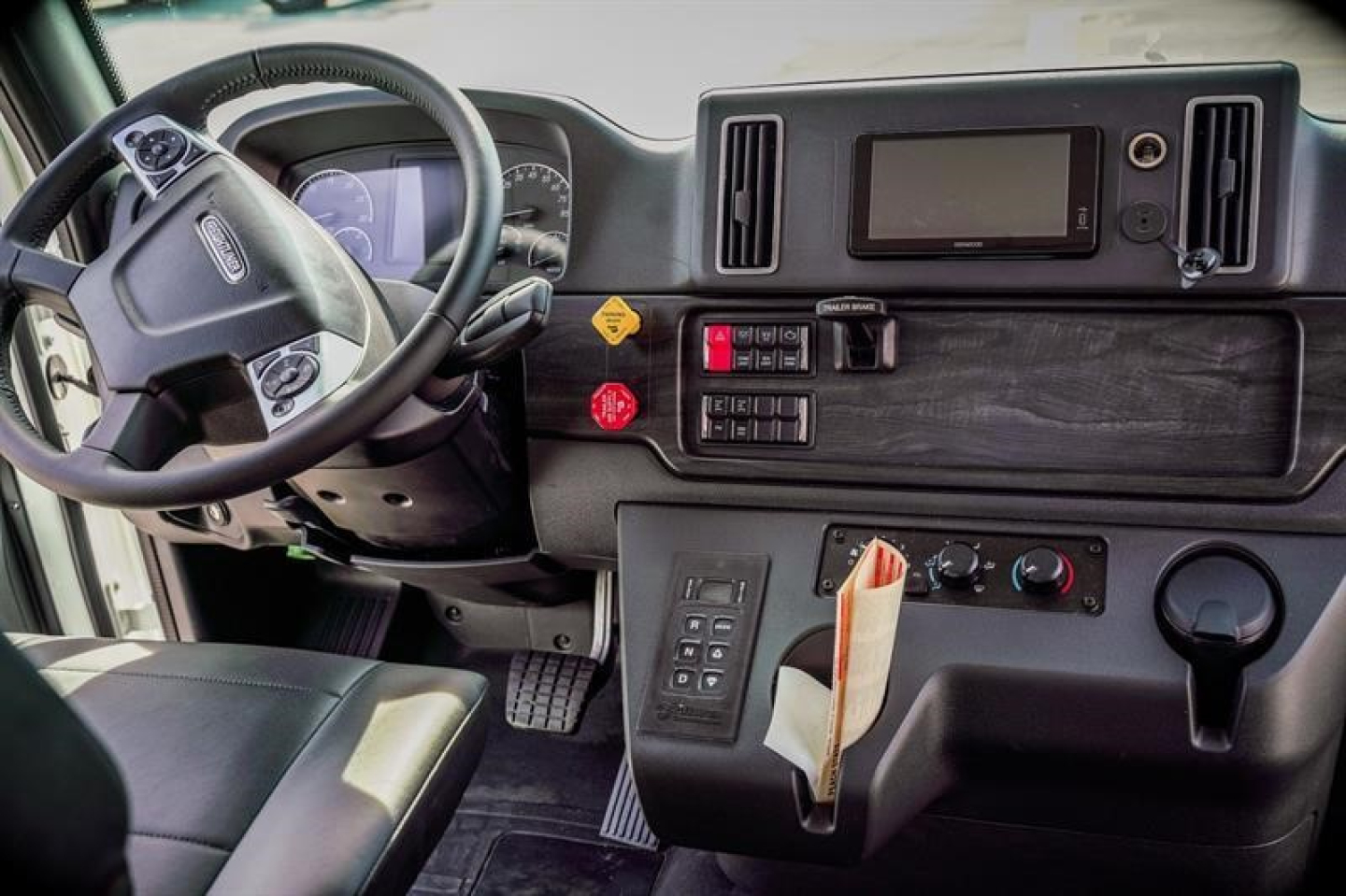 Cab and chassis interior: steering wheel, dashboard with digital display, control panel, gear shifter, and cloth seat in view.