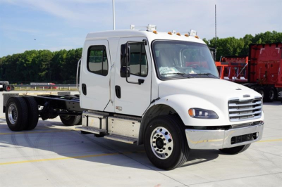 Freightliner M2 106 Plus cab and chassis truck in white, side view showing dual crew cab doors, metal step boards, and chassis behind cab.