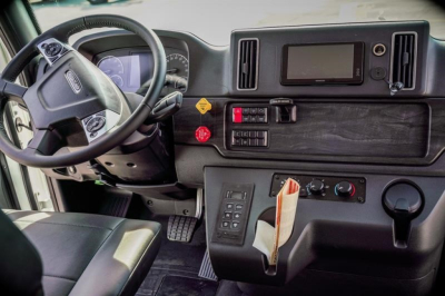 Cab and chassis interior: steering wheel, dashboard with digital display, control panel, gear shifter, and cloth seat in view.