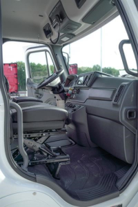 Cab interior of a Freightliner M2 106 Plus truck from the driver's side, showing steering wheel, dashboard, seats, and overhead console.