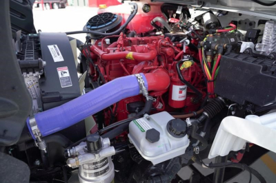 Freightliner M2 106 Plus engine bay showing red engine, purple intercooler hose, coolant reservoir, and various hoses and wiring.