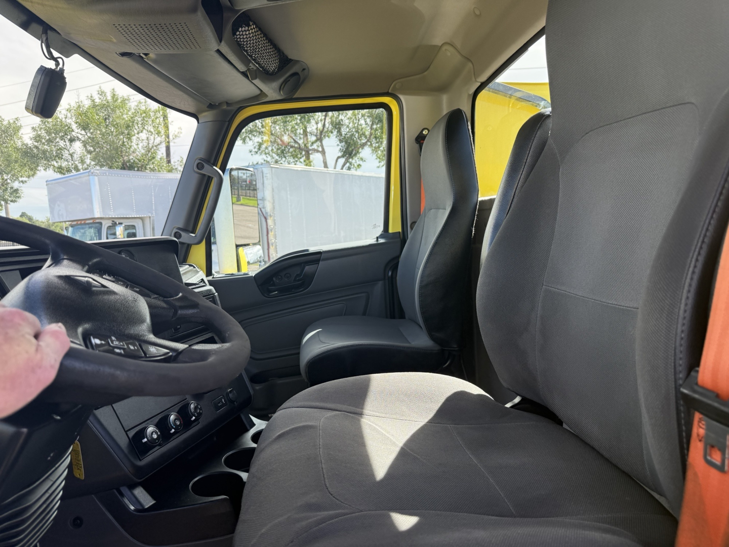 Interior of a 2023 International LT625 cab showing steering wheel, dashboard, driver seat, and passenger seat. Yellow exterior visible through window.